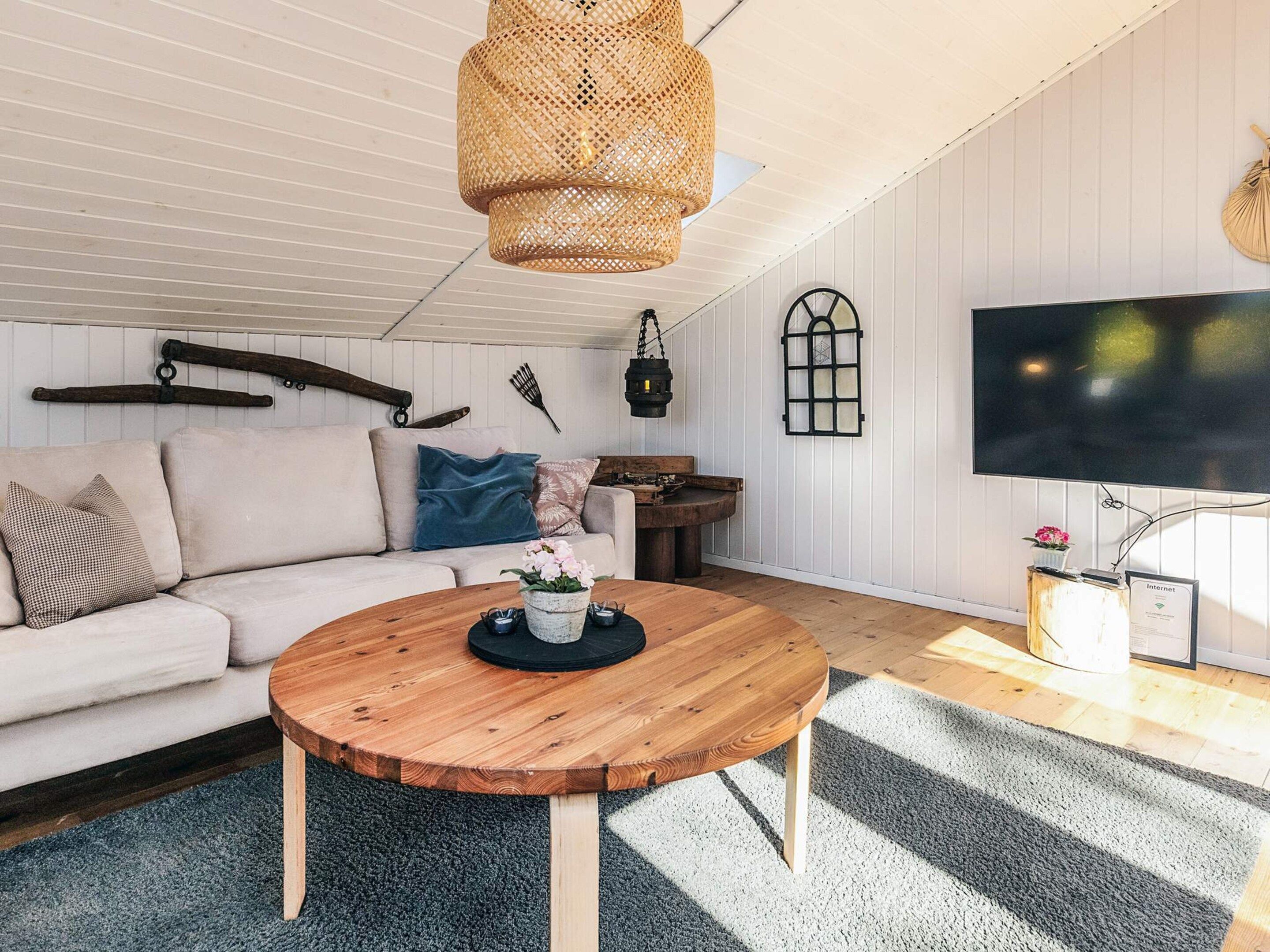 Un salon chaleureux avec une table basse en bois, un canapé blanc, un téléviseur et un luminaire suspendu en osier.