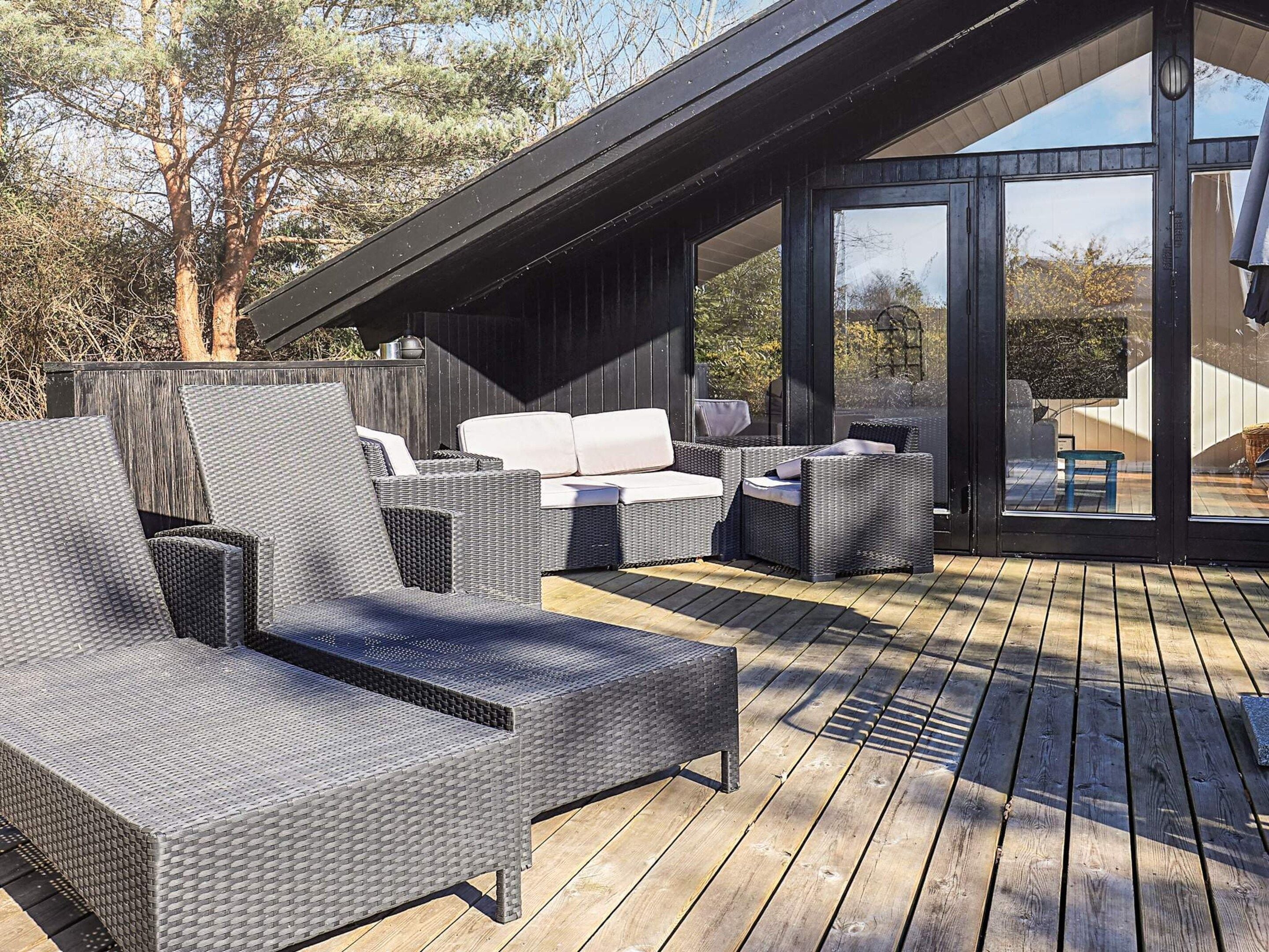 An outdoor deck with wicker furniture, including a sofa and chairs, and a wooden floor.