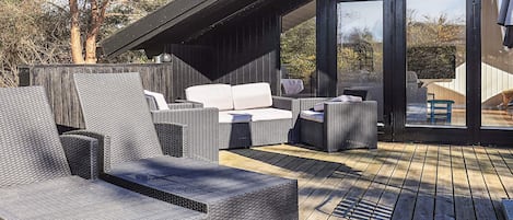 An outdoor deck with wicker furniture, including a sofa and chairs, and a wooden floor.