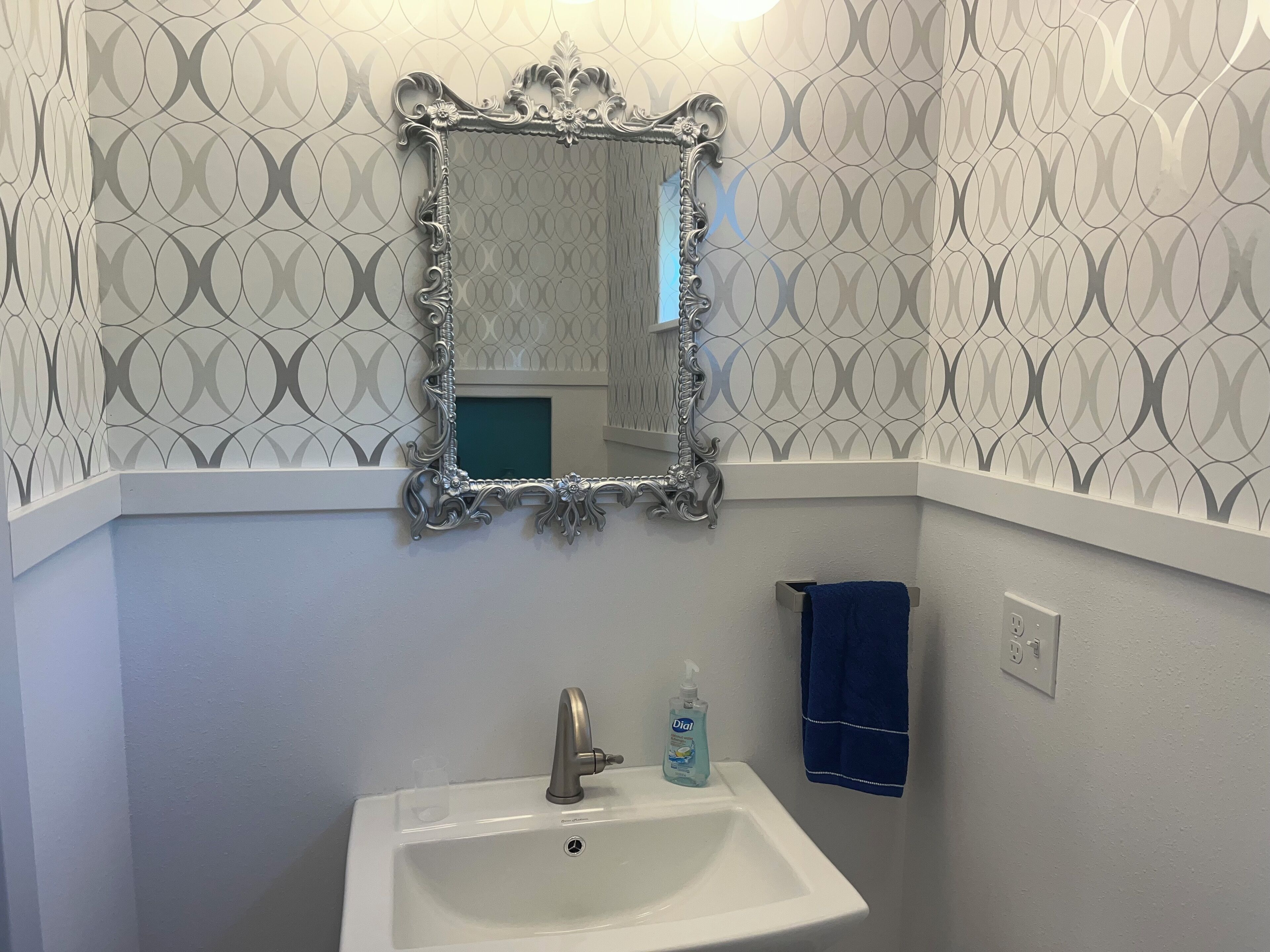 A bathroom with a white sink, a mirror with an ornate frame, a blue towel, and a bottle of hand soap.