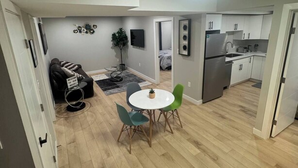 A modern kitchen with white cabinets and stainless steel appliances, a dining area with a round table and chairs, and a cozy seating area with a sofa and a small rug. - Cozy 3BR Suite at Winnipeg South (Winnipeg)