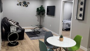 A modern living room with a round table, two chairs, a sofa, a TV, and a decorative wall piece. - Cozy 3BR Suite at Winnipeg South (Winnipeg)
