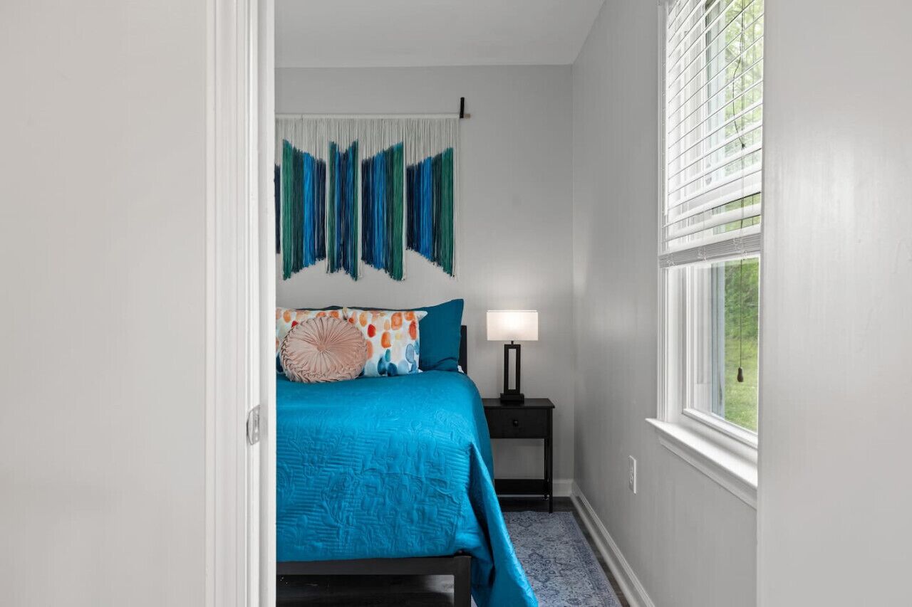 A bedroom with a bed, a nightstand, a lamp, and a window.