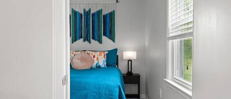 A bedroom with a bed, a nightstand, a lamp, and a window.