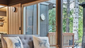 A wooden-framed sofa with two cushions, a wooden coffee table, and a large window with a view of trees. - Relaxing, Private Cabin w/Hot Tub & Generator near Mt Rainier! (Ashford)