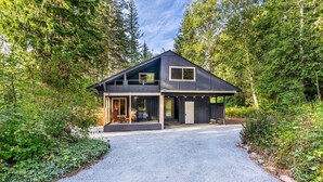 A modern house with a gravel driveway, surrounded by dense forest. - Relaxing, Private Cabin w/Hot Tub & Generator near Mt Rainier! (Ashford)