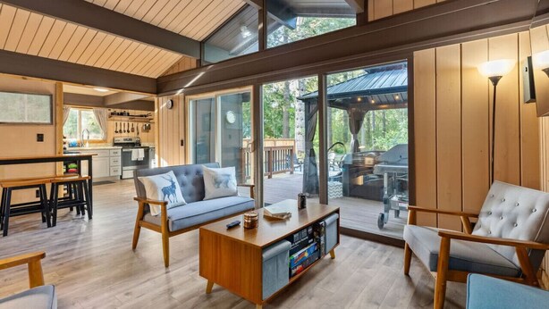 A spacious living area with a sofa, chairs, a coffee table, and a kitchen in the background. - Relaxing, Private Cabin w/Hot Tub & Generator near Mt Rainier! (Ashford)