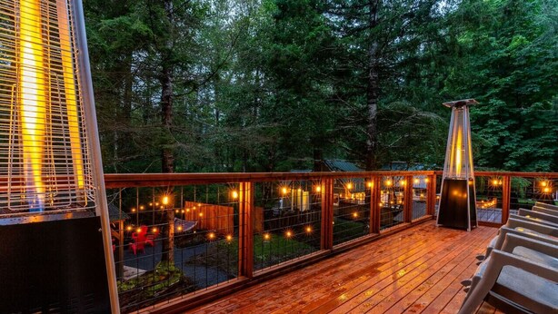 A wooden deck with a railing, outdoor seating, and a view of a forested area.