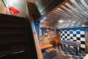 A room with a foosball table, a checkered sofa, and a wooden staircase.