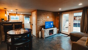 A cozy room with a wooden interior, a television, a fireplace, and a dining area with a chessboard. - Mt Rainier Cabin! Sauna, Game Rm, Hot Tub, Firepit (Ashford)