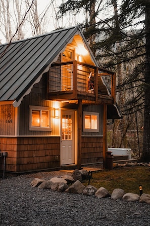 A two-story wooden cabin with a balcony, a front door, and a mailbox.