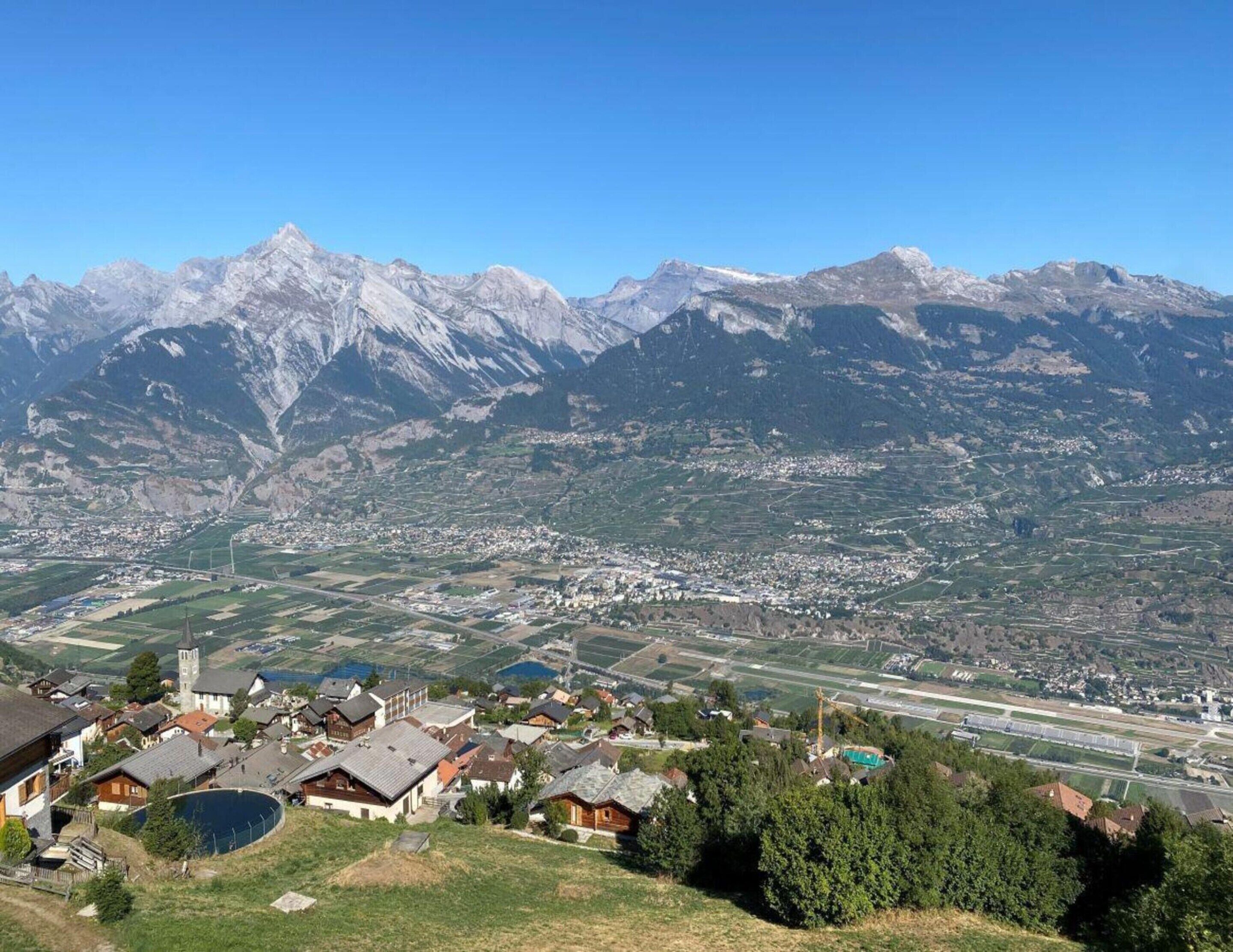 A mountainous landscape with a valley town featuring houses, a church, and a clear view of the mountains.