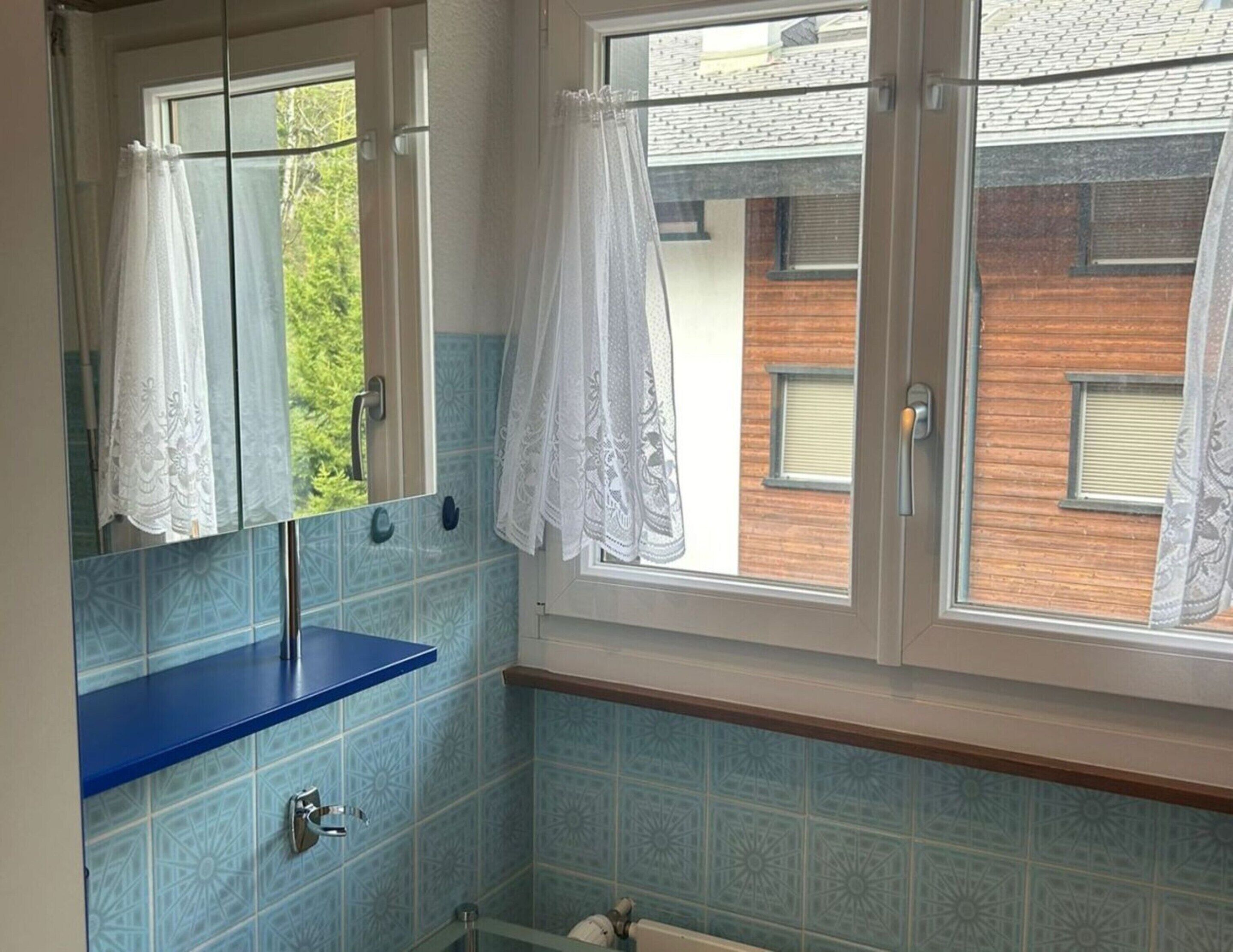 Ein Badezimmer mit blauem Waschbecken, einem Spiegel und einem Fenster mit Spitzenvorhängen.