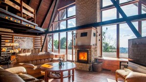 A spacious living room with a stone fireplace, leather sofas, and large windows offering a view of the outdoors. - Comfortable Villa With Facilities (Benecko)