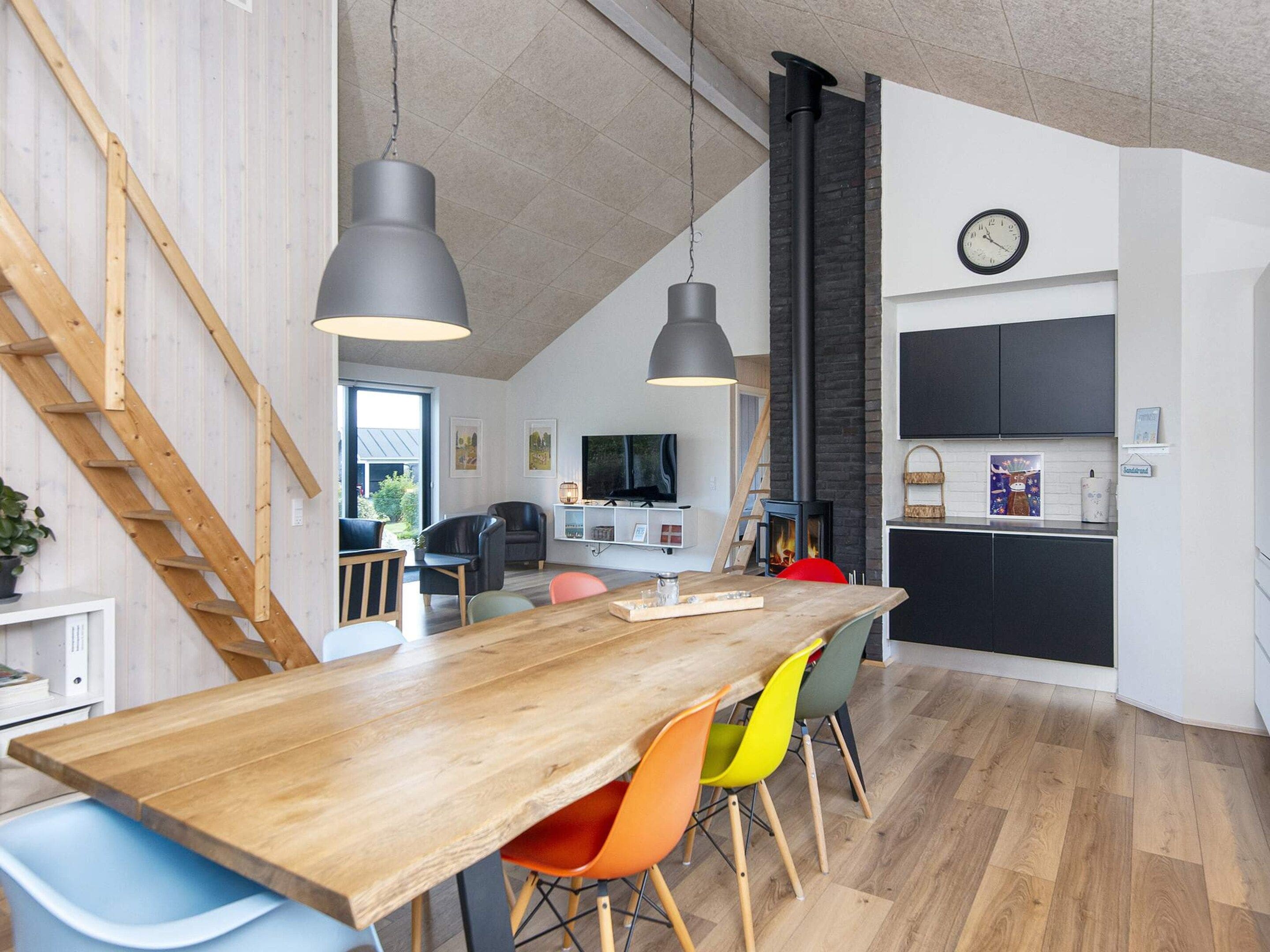 Eine moderne Küche mit einem Holztisch, bunten Stühlen, einem eingebauten Herd und einer Uhr an der Wand.