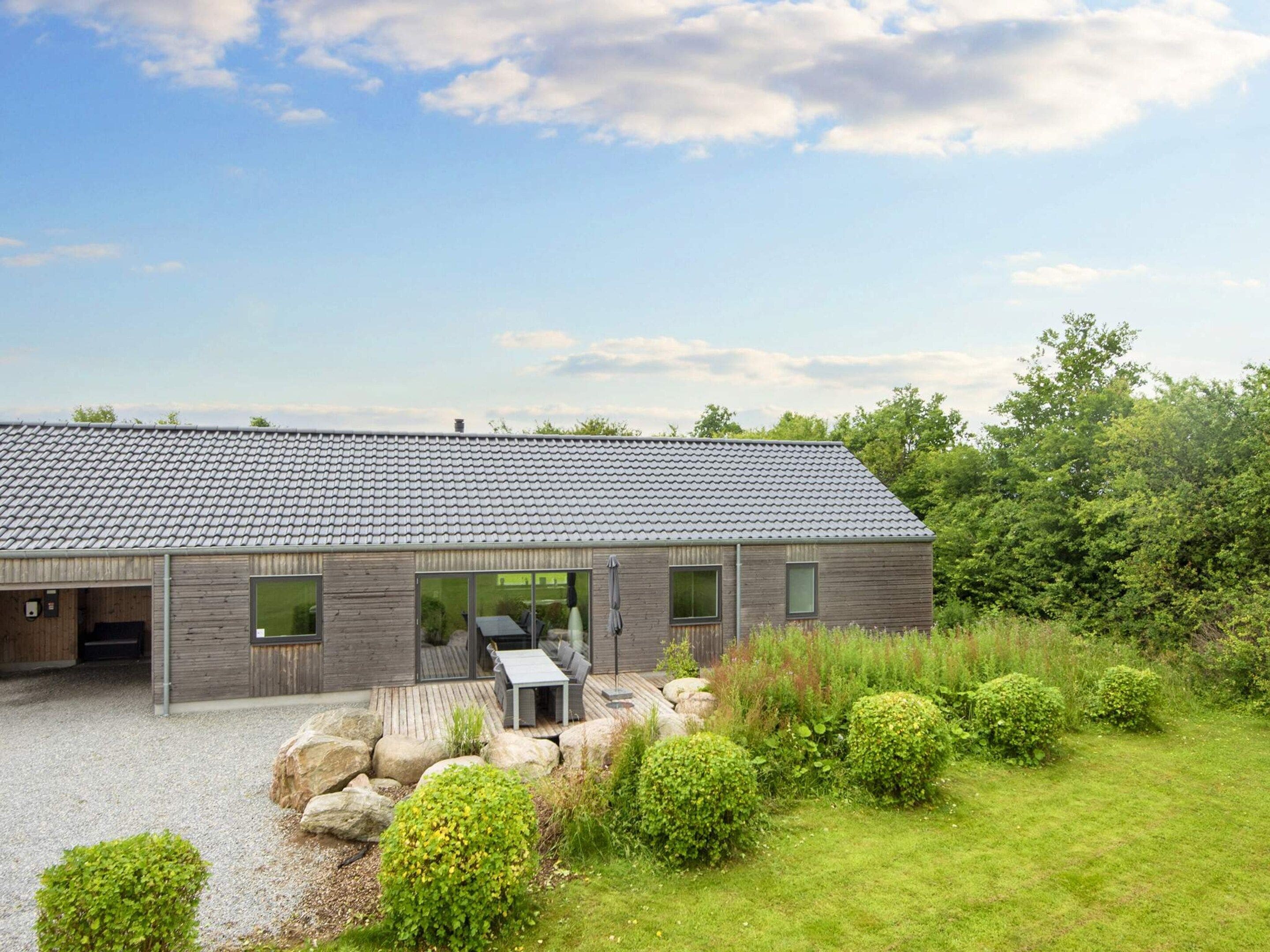Ein modernes Gebäude mit geneigtem Dach, großen Fenstern und einer Terrasse mit Gartenmöbeln.