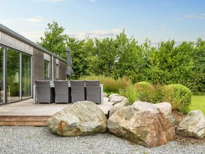 A modern outdoor deck with wicker furniture and a large umbrella, surrounded by a natural landscape with rocks and greenery. - 4 Star Holiday Home in Sydals (Sydals)