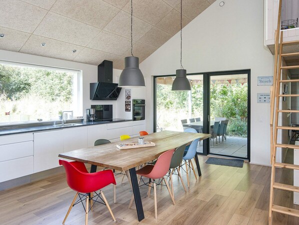 A modern kitchen with a wooden table and colorful chairs, a built-in oven, and a large window.