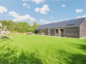 A modern house with a large lawn, a wooden play structure, and a covered patio area. - 4 Star Holiday Home in Sydals (Sydals)