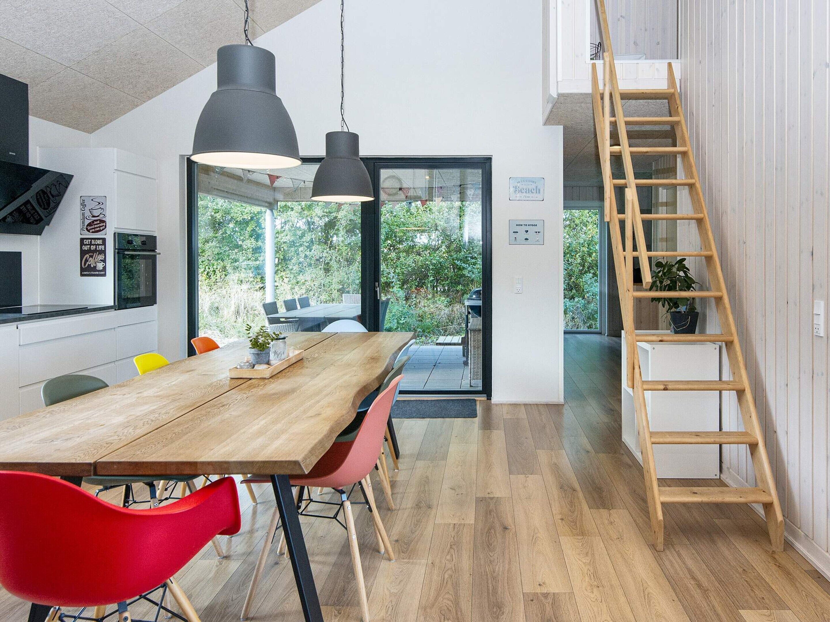 A modern kitchen with a wooden dining table, red chairs, and pendant lighting.