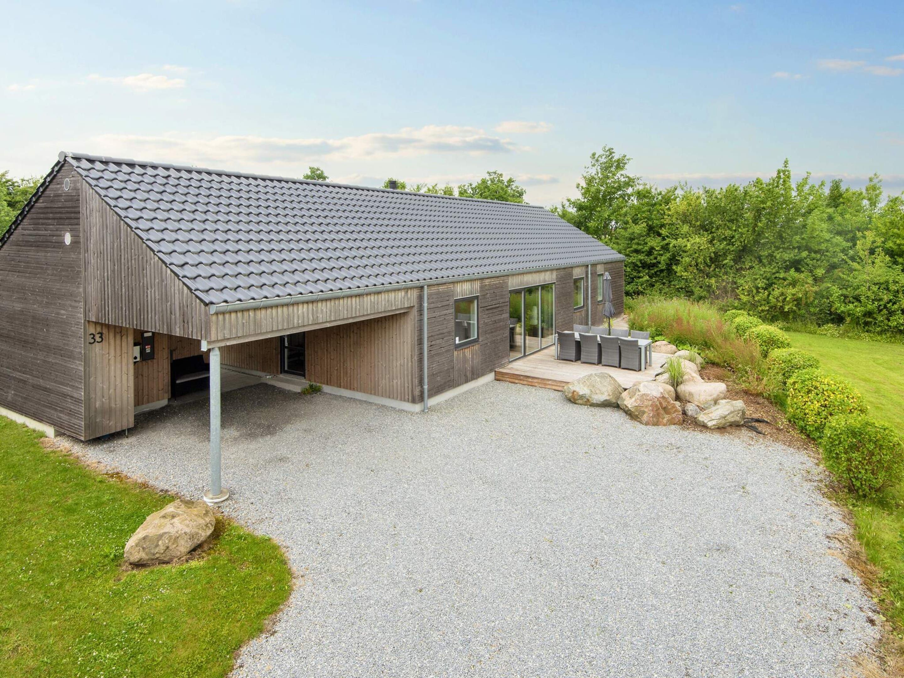 A modern building with a sloped roof, a covered patio area, and a gravel driveway.