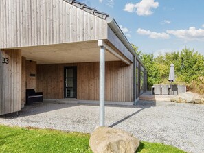 A modern building with a wooden exterior, a covered entrance area, and a seating arrangement outside. - 4 Star Holiday Home in Sydals (Sydals)