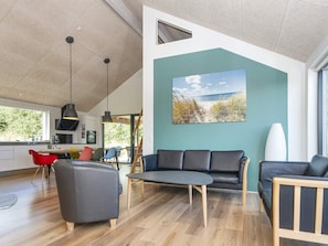 A modern living room with a large window, a dining area with colorful chairs, and a kitchen in the background.