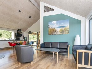 A modern living room with a large window, a dining area, and a kitchen in the background.