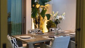 A dining table set with plates, cutlery, and wine glasses, surrounded by wicker chairs.