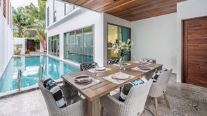 A dining area with a pool view, wooden ceiling, and modern furnishings.
