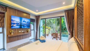 A hotel room with a large bed, a flat-screen TV mounted on the wall, a small table with a vase of flowers, and a view of the outdoors through large windows.