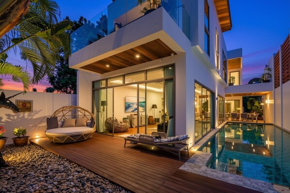 Una casa moderna con un patio de cristal, piscina y terraza de madera.