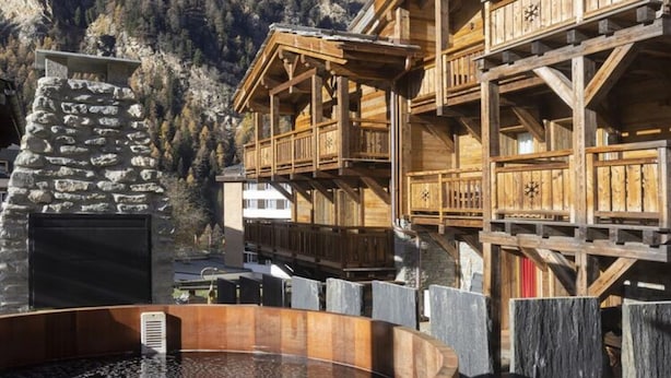A wooden chalet with a stone fireplace, wooden balconies, and a hot tub.