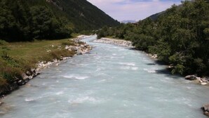 A river flowing through a mountainous area with rocky banks and dense greenery on both sides.