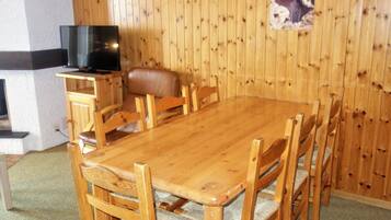 A wooden dining table with six chairs, a leather sofa, and a television on a wooden stand.