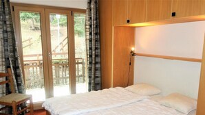 A double bed with a wooden headboard, a chair, and a view of an outdoor deck through a glass door. - Mystical Apartment With Mountain Views (Veysonnaz)