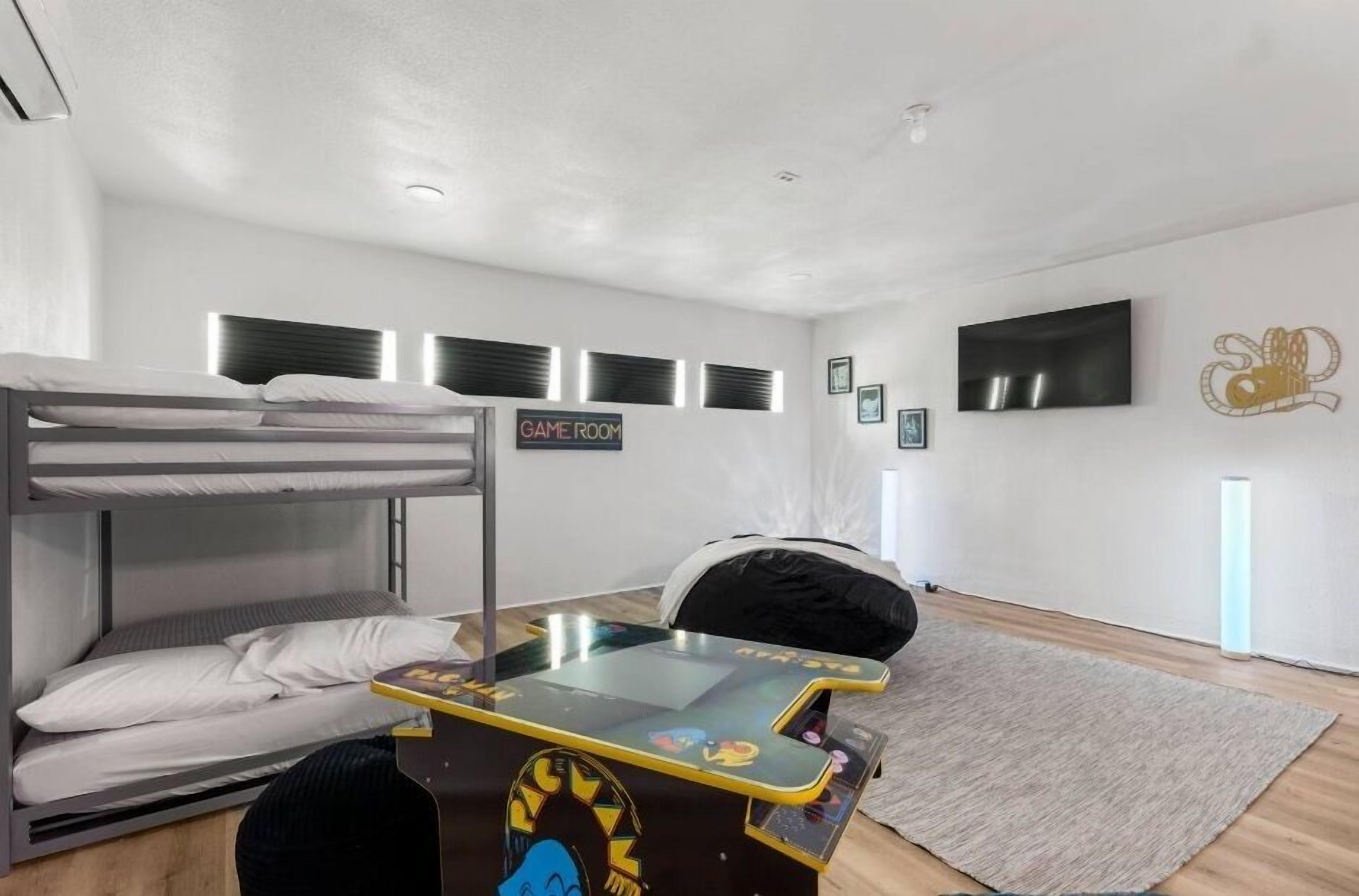 Habitación con literas, una mesa de juegos, un televisor y un letrero que dice 'GAME ROOM'.