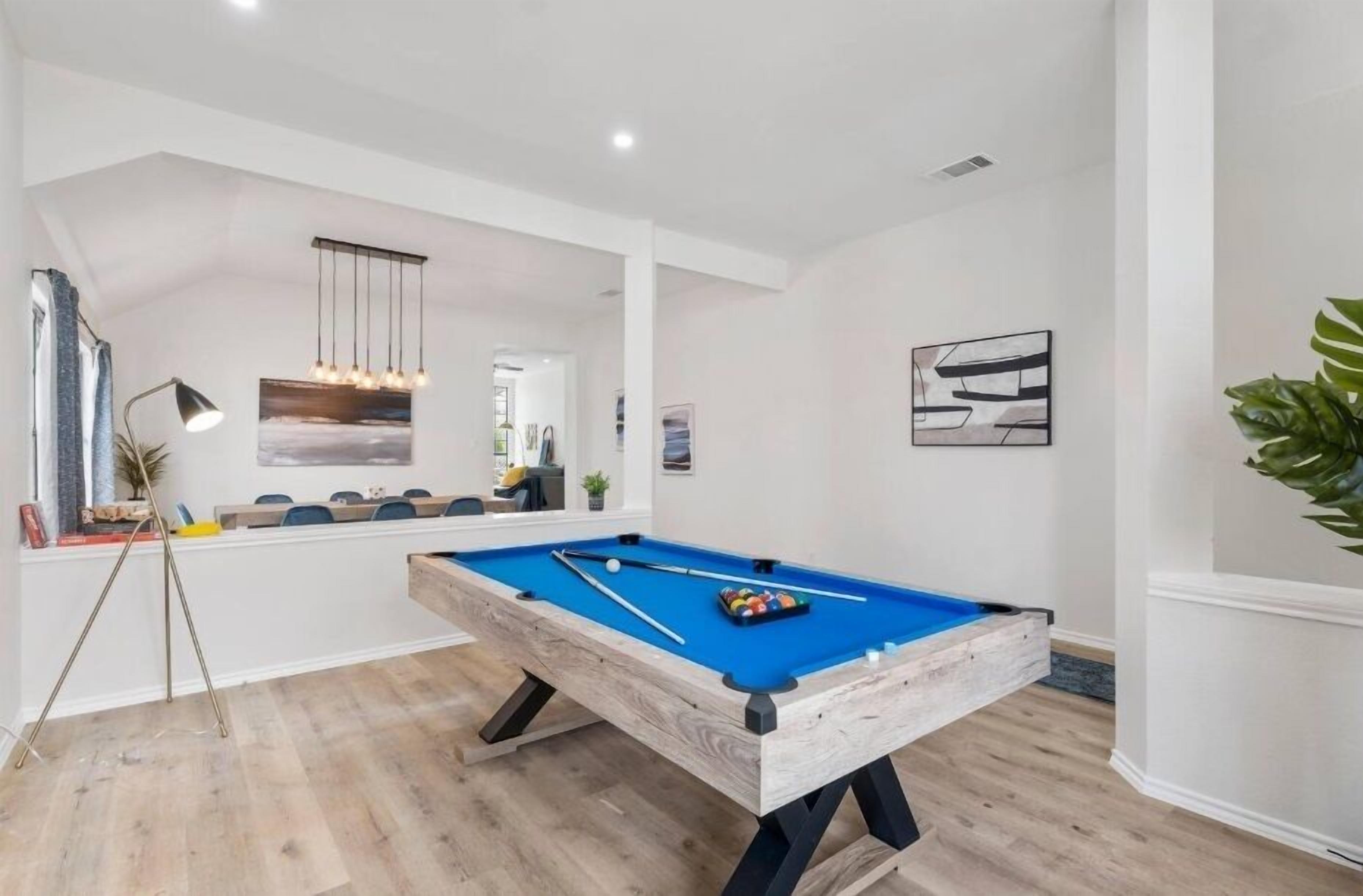 A pool table in a modern room with white walls and wooden flooring.
