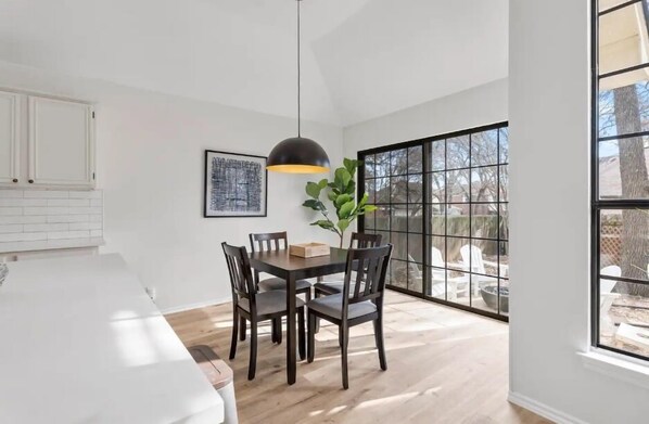 A dining area with a table and chairs, a pendant light, a framed artwork, and a view through large windows. - The Bonnie - 5 Bed Near Everything (Cedar Park)