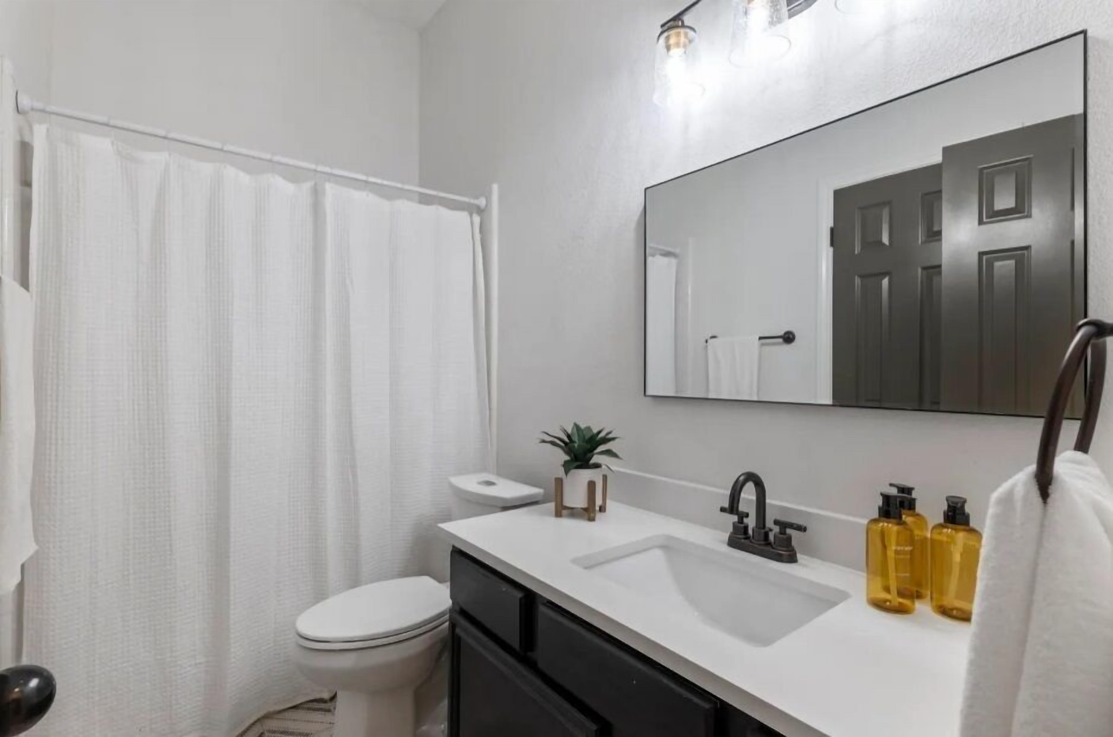 A modern bathroom with a white toilet, a white sink, a mirror, and a shower curtain.