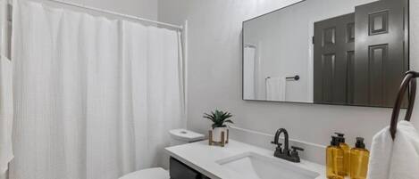 A modern bathroom with a white toilet, a white sink, a mirror, and a shower curtain.