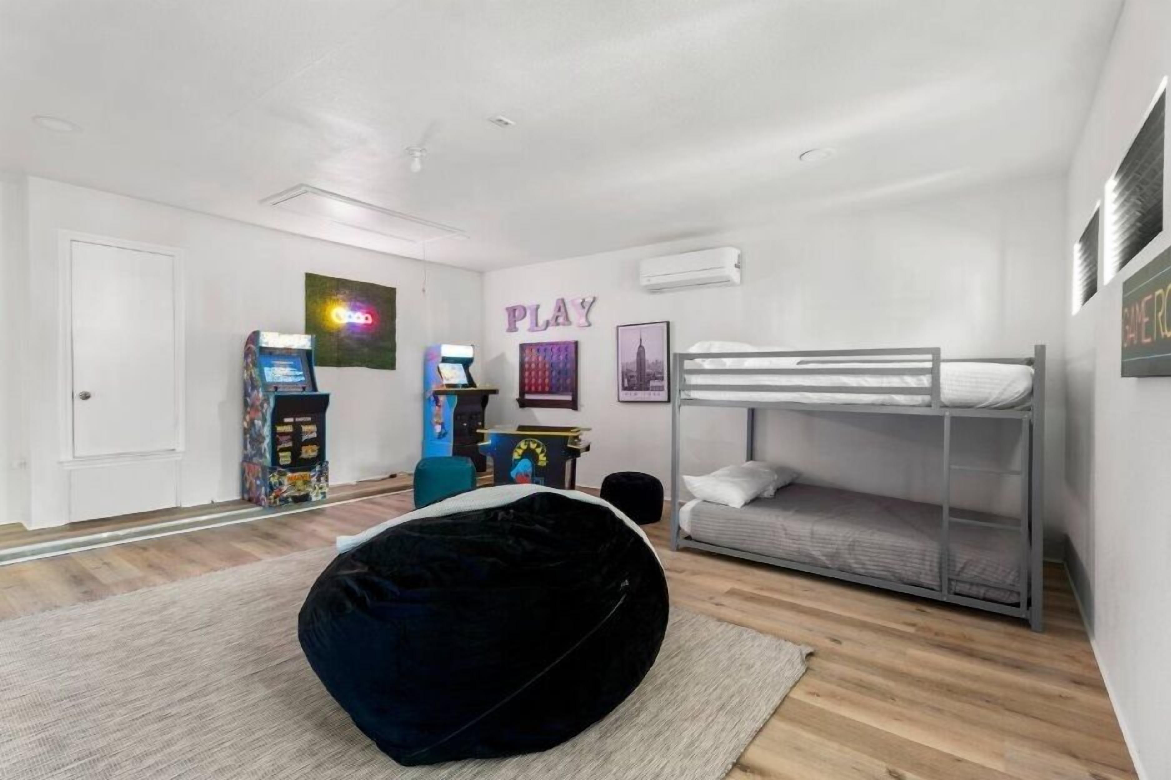 A modern bedroom with a bunk bed, a bean bag chair, a gaming console, and a wall with the word "PLAY".