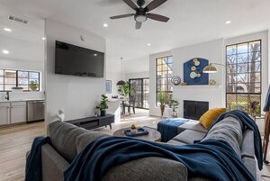 Una sala de estar moderna con sofá, mesa de centro y chimenea. Hay un televisor montado en la pared y un ventilador de techo.