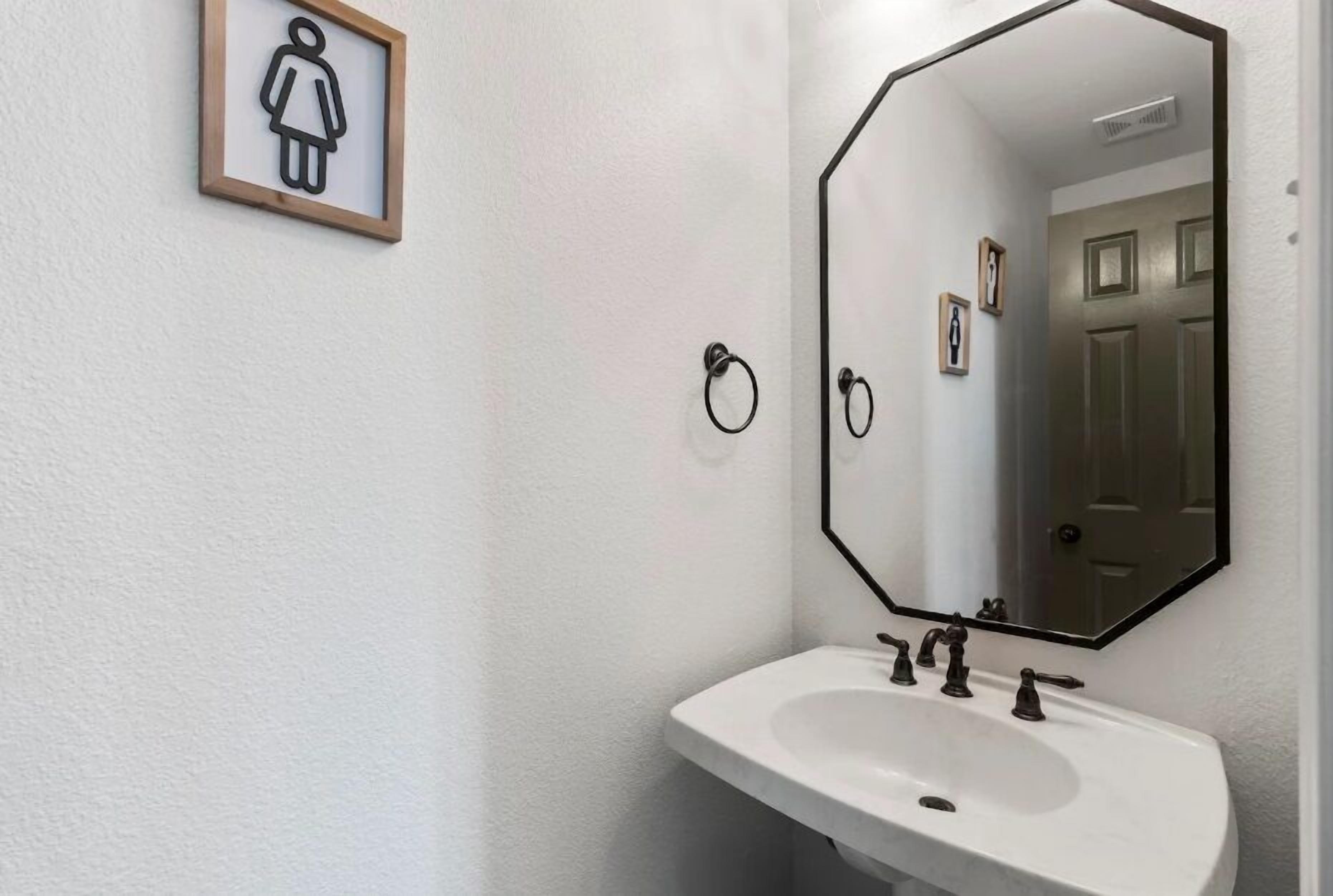 Une salle de bain avec un lavabo blanc, un grand miroir et un panneau indiquant les toilettes.