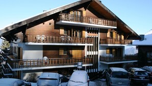 A multi-story wooden building with balconies, parked cars, and a snowy environment.