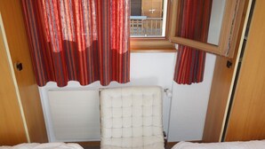 A small room with two beds, a cushioned chair, and red curtains.