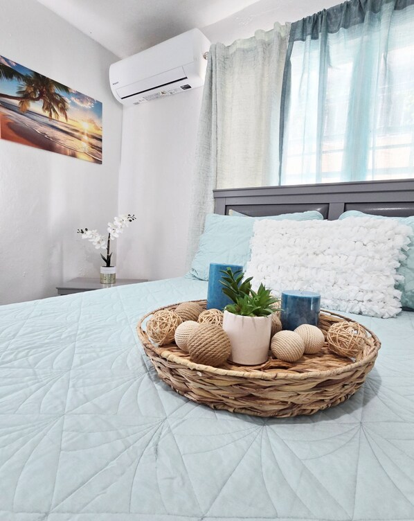 Un letto rifatto con una coperta azzurra, un cesto di vimini con oggetti decorativi e un condizionatore d'aria a parete.