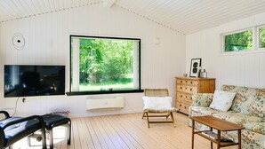 A room with a large window, a flat-screen TV, a wooden bench, a sofa, and a wooden dresser. - 8 Person Holiday Home in Asnaes (Asnaes)