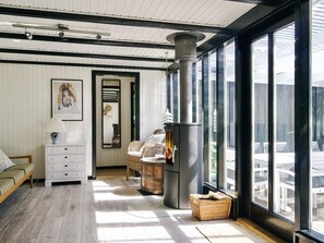 A cozy room with a large window, a fireplace, wicker furniture, and a white dresser. - 8 Person Holiday Home in Asnaes (Asnaes)