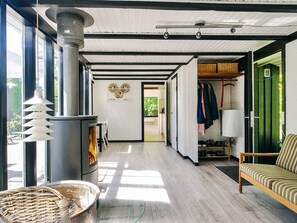 Een modern interieur met een houtkachel, een eethoek met stoelen, een bank en een kledingrek.